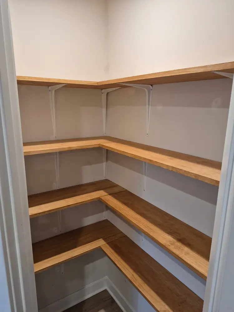 Finished oak pantry shelving wrapping two walls of the closet